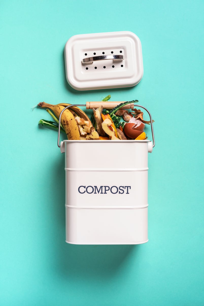 Recycle Kitchen Waste. Sustainable and Zero Waste Living. Vegetable Waste in Recycling Compost Pot. Top View. Copy Space. Peeled Vegetables on Chopping Board, White Compost Bin on Blue Background.